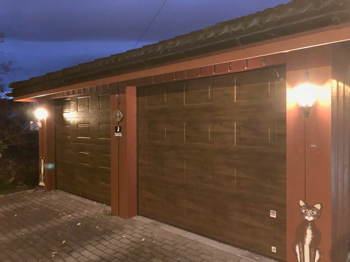 Dobbel garasje i skumringen med to tente vegglamper ved portene