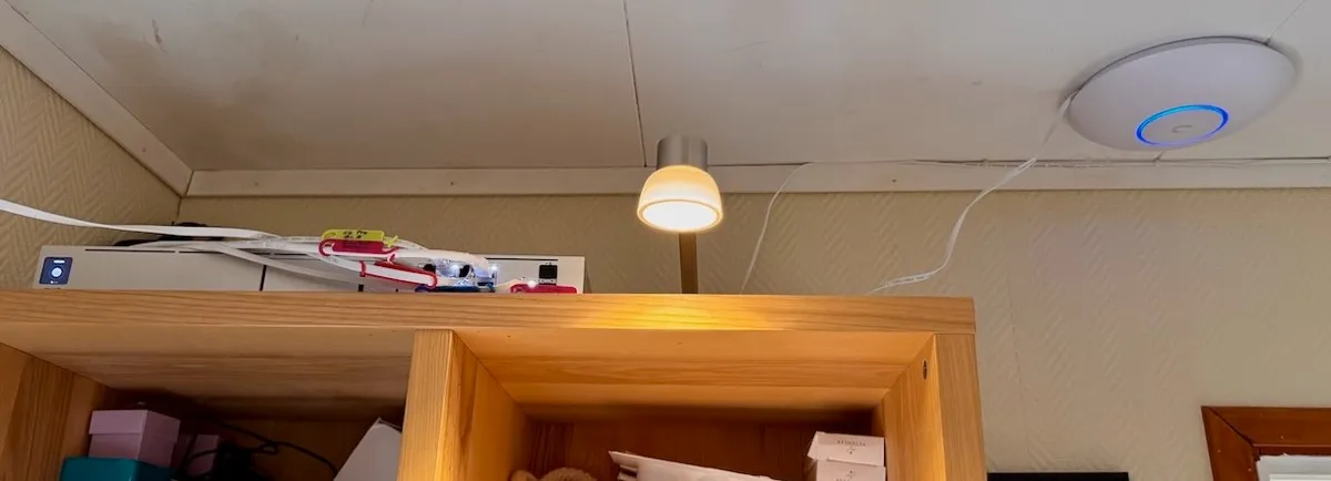 UniFi Dream Machine SE ruter, plassert høyt på en bokhylle, samt U7 aksesspunkt montert i taket