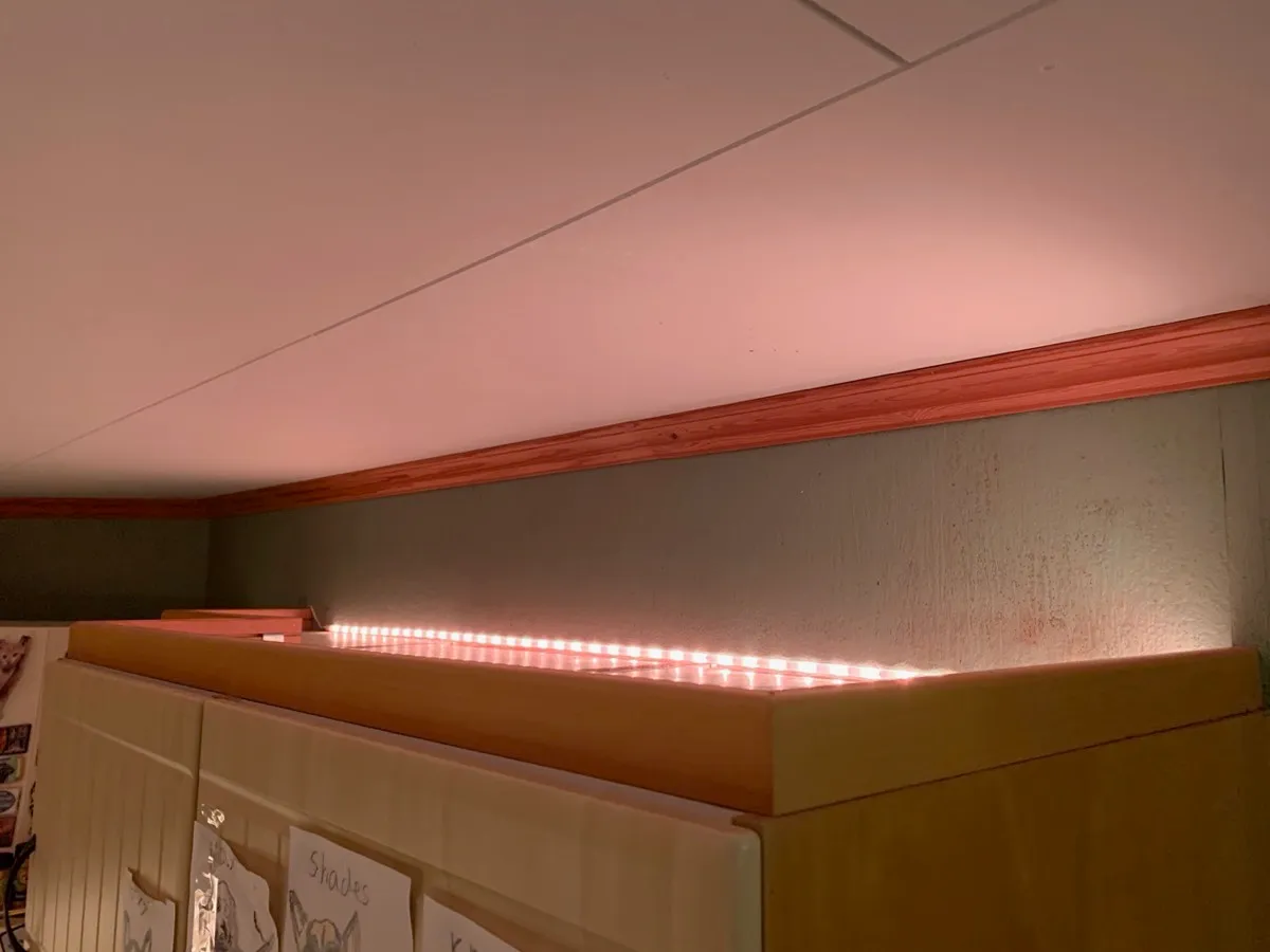 Nærbilde av en lysstripe som ligger oppå et overskap og lyser rosa opp mot veggen og taket