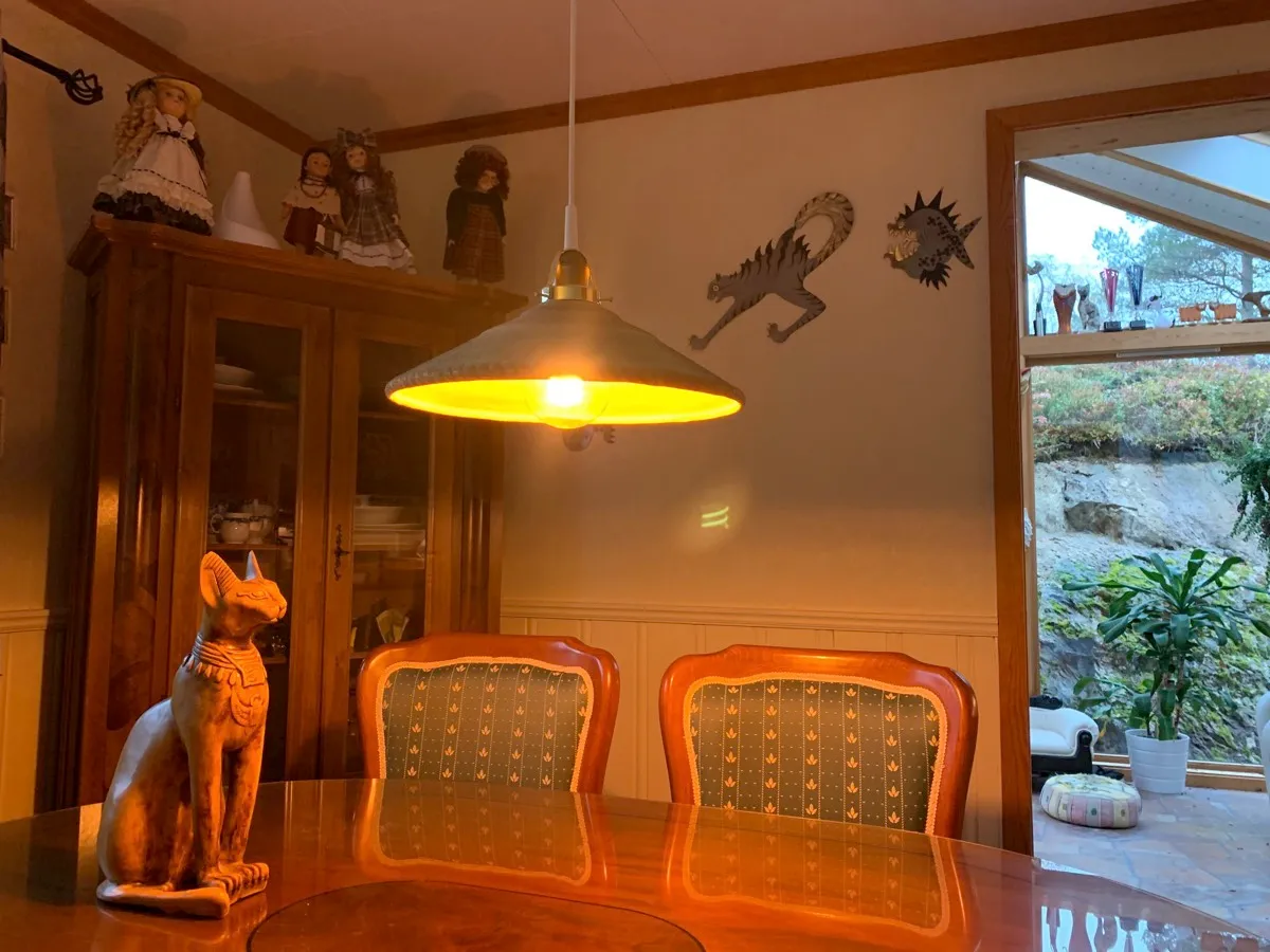Spisebordslampen med grønn skjerm tent over spisebordet, med et glasskap og to stoler i bakgrunnen