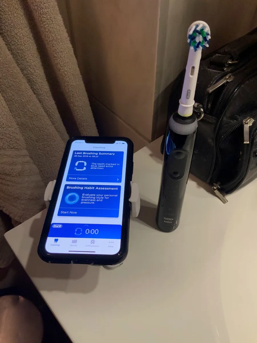 Til venstre, Oral-B tannbørsten og sugekorppholderen (som monteres på speilet over vasken ved bruk), til høyre, skjermbilde fra Oral-B appen og status for børstingen