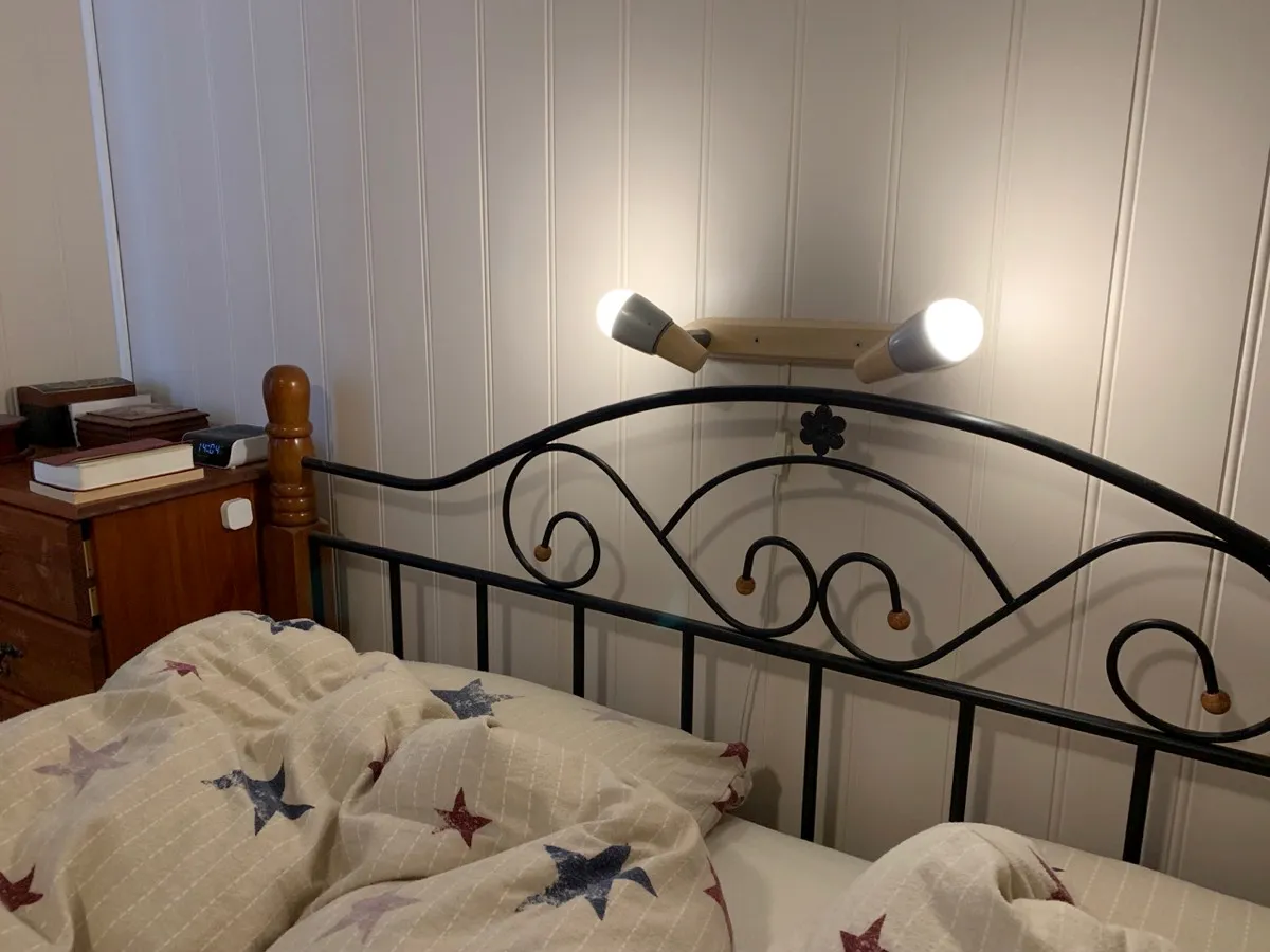 Lampe over senger med to Trådfri-pærer og en bryter på hvert nattbord. Til høyre vises Lenovo smart klokke og HomePod Mini samt et par andre fjernkontroller/brytere
