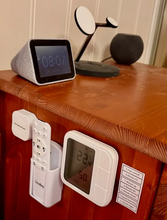 Lampe over senger med to Trådfri-pærer og en bryter på hvert nattbord. Til høyre vises Lenovo smart klokke og HomePod Mini samt et par andre fjernkontroller/brytere