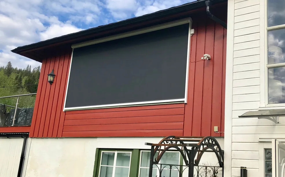 Solskjerm som dekker tre stuevinduer, med Sonneboy sol-/vindstyring til høyre for vinduene